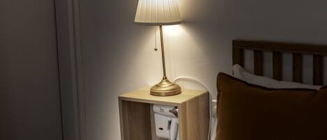 A bedside table with a lamp, a phone, and a wooden headboard.