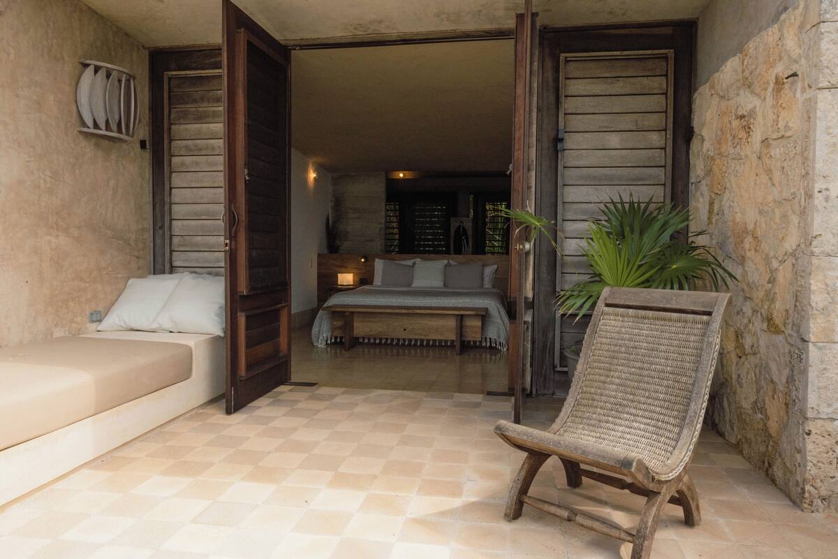 An open-plan bedroom with a bed, a sofa, a chair, and a view into the living area.