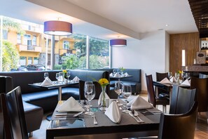 A restaurant with tables set for dining, a view of the outside, and a bar area.