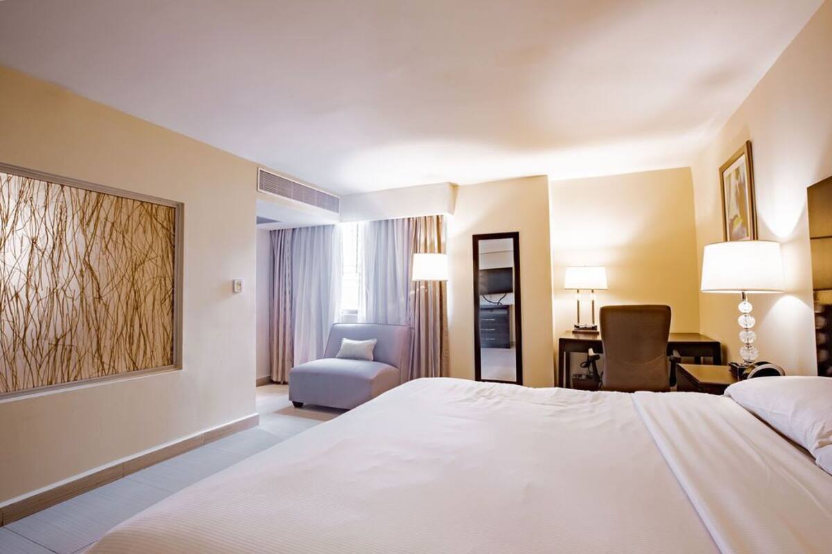 A hotel room with a large bed, a desk with a chair, a mirror, and a window with curtains.