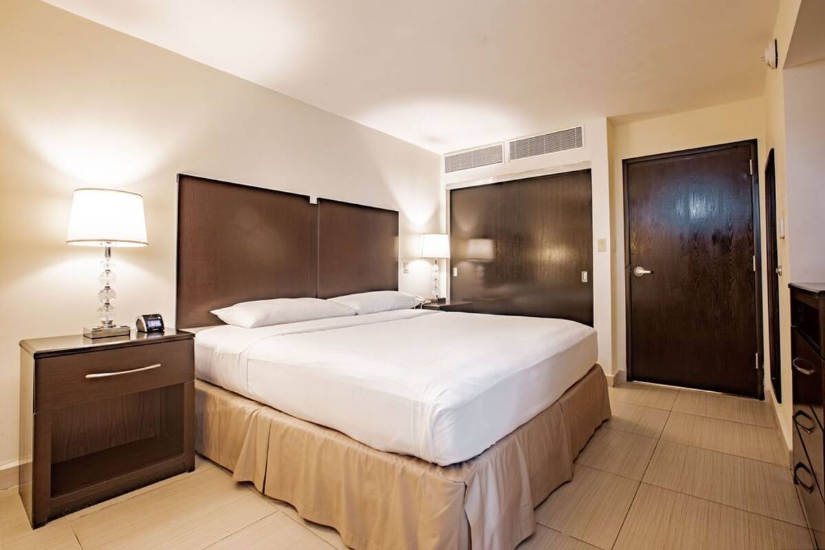 A hotel room with a large bed, two bedside tables with lamps, a wardrobe, and a door.