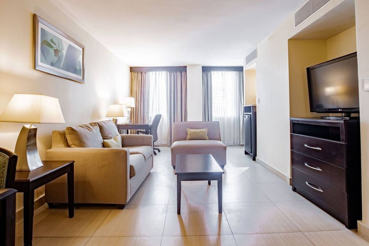 A hotel room with a sofa, a coffee table, a TV, and a cabinet.