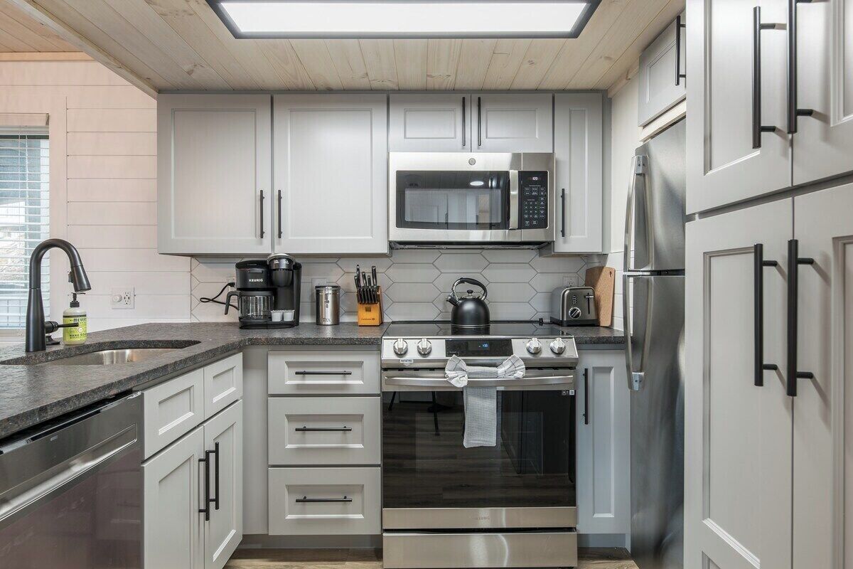 A modern kitchen with stainless steel appliances, white cabinetry, and a black countertop.