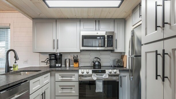 Une cuisine moderne dotée d’appareils électroménagers en acier inoxydable, de meubles blancs et d’un plan de travail noir.