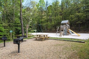 A playground with swings, a slide, and a picnic table in a wooded area. - Mountain Views Indoor Pool Access Sauna Access (Gatlinburg)