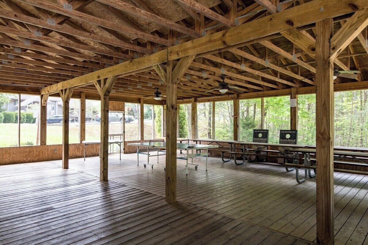 An open pavilion with a wooden floor and ceiling, picnic tables, and a view of the outdoors.