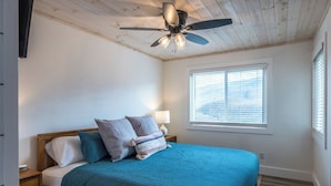 Une chambre à coucher avec un lit, un ventilateur de plafond, une fenêtre avec des stores et une table de chevet.