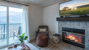 Un salon avec une cheminée, un téléviseur, un fauteuil confortable et une vue sur l’extérieur.