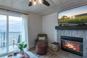 A living room with a fireplace, a television, a comfortable chair, and a view of the outdoors. - Mountain Views Indoor Pool Access Sauna Access (Gatlinburg)