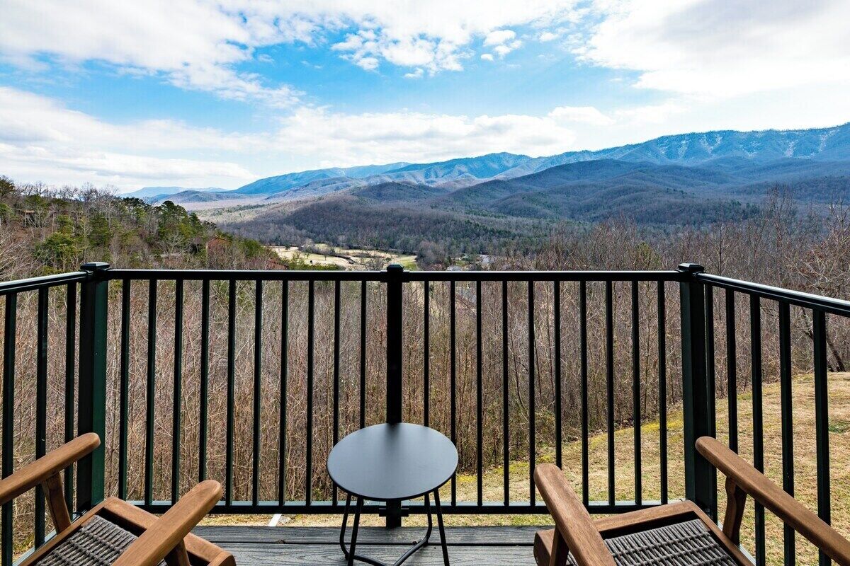 A balcony with a table and chairs, overlooking a mountainous landscape.