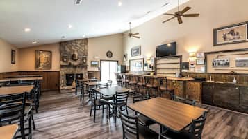 A restaurant with multiple tables and chairs, a stone fireplace, and a bar area.
