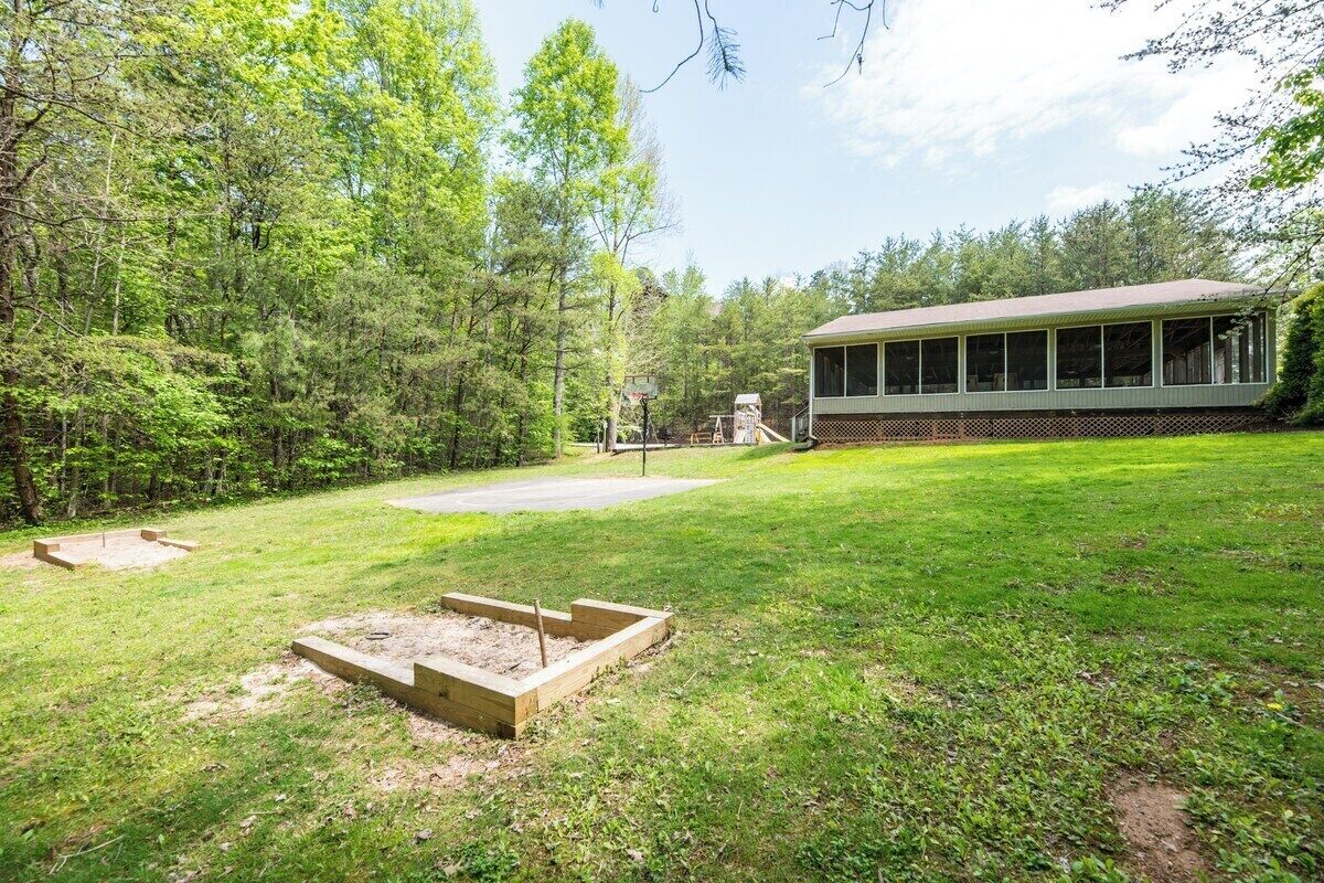 A backyard with a wooden deck, a basketball hoop, and a house with a large windowed porch.