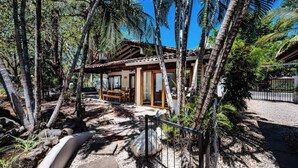 Una casa de estilo tropical con un patio, rodeada de palmeras y un camino de entrada de grava.