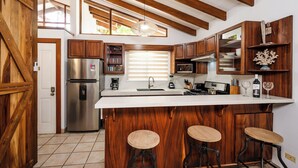 Una cocina con armarios de madera, un refrigerador de acero inoxidable, una encimera blanca y una zona de bar con taburetes.
