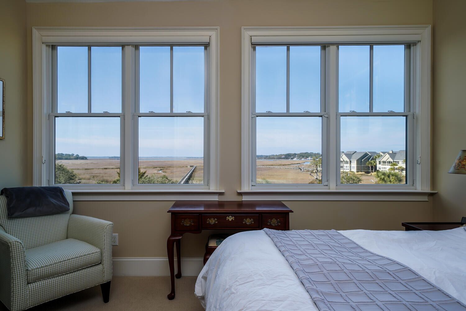 A bedroom with two large windows offering a view of a field and distant buildings.
