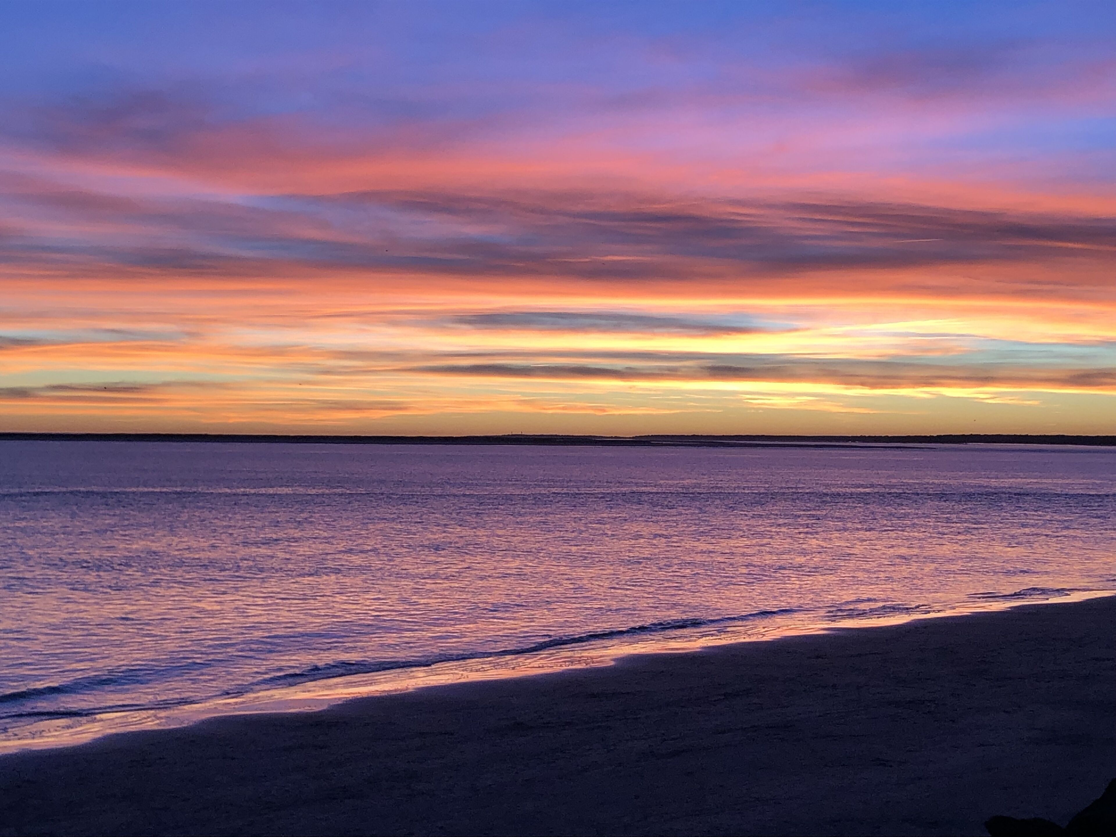 Una playa con un atardecer sobre el agua.