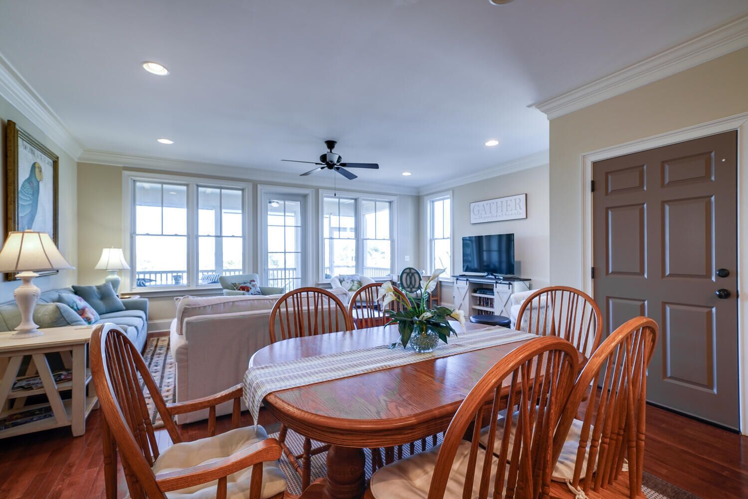 A spacious dining area with a wooden table and chairs, a ceiling fan, and a television in the background.