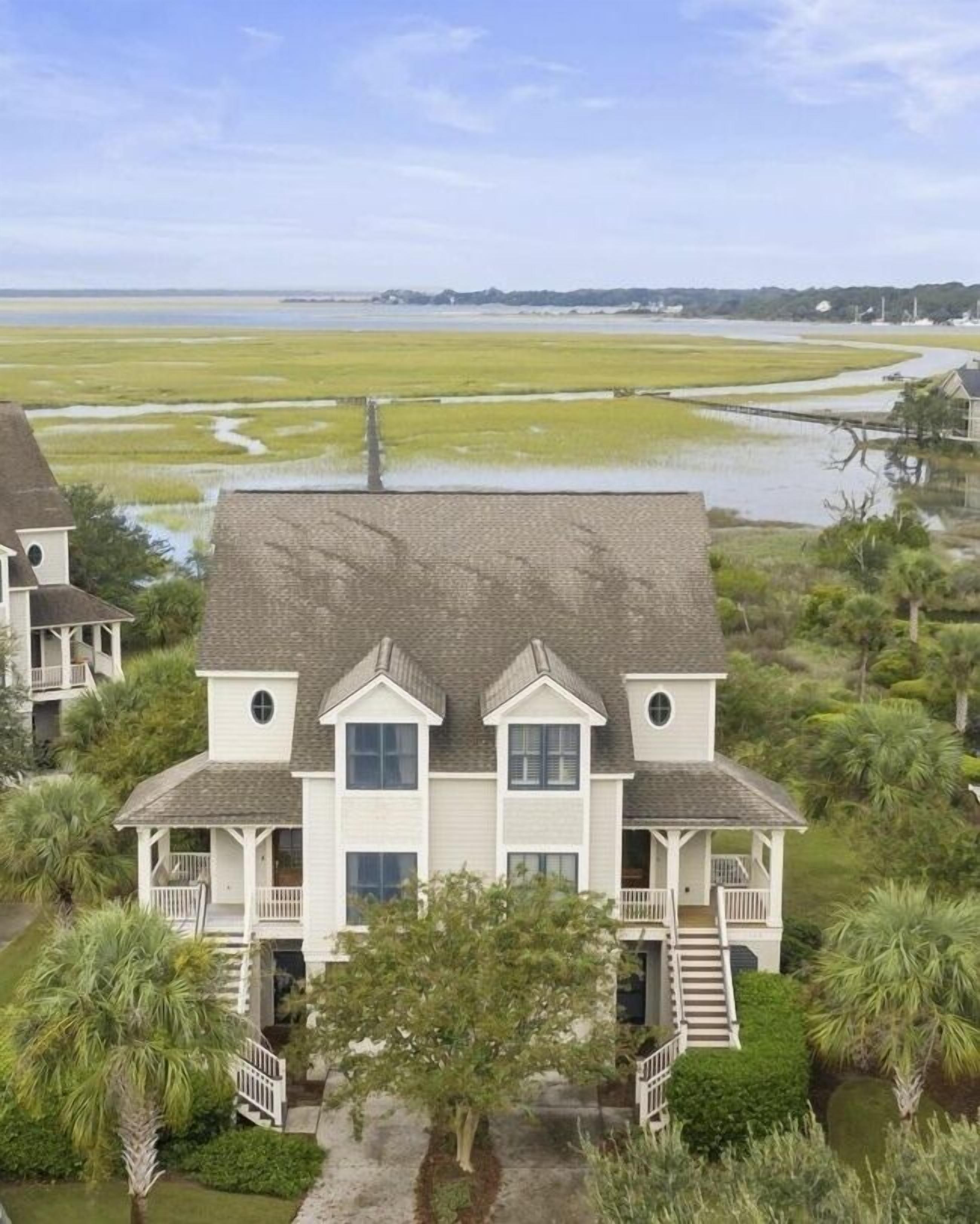 A large, two-story house with a covered porch and a staircase leading to the second floor. The house is surrounded by lush greenery and a view of a marshy landscape.