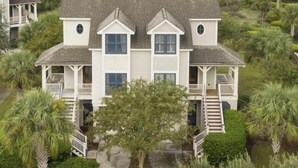 A large, two-story house with a covered porch and a staircase leading to the second floor. The house is surrounded by lush greenery and a view of a marshy landscape. - Stunning Gem! Amazing Marsh/Tidal Views. Amenity access included! (Seabrook Island)