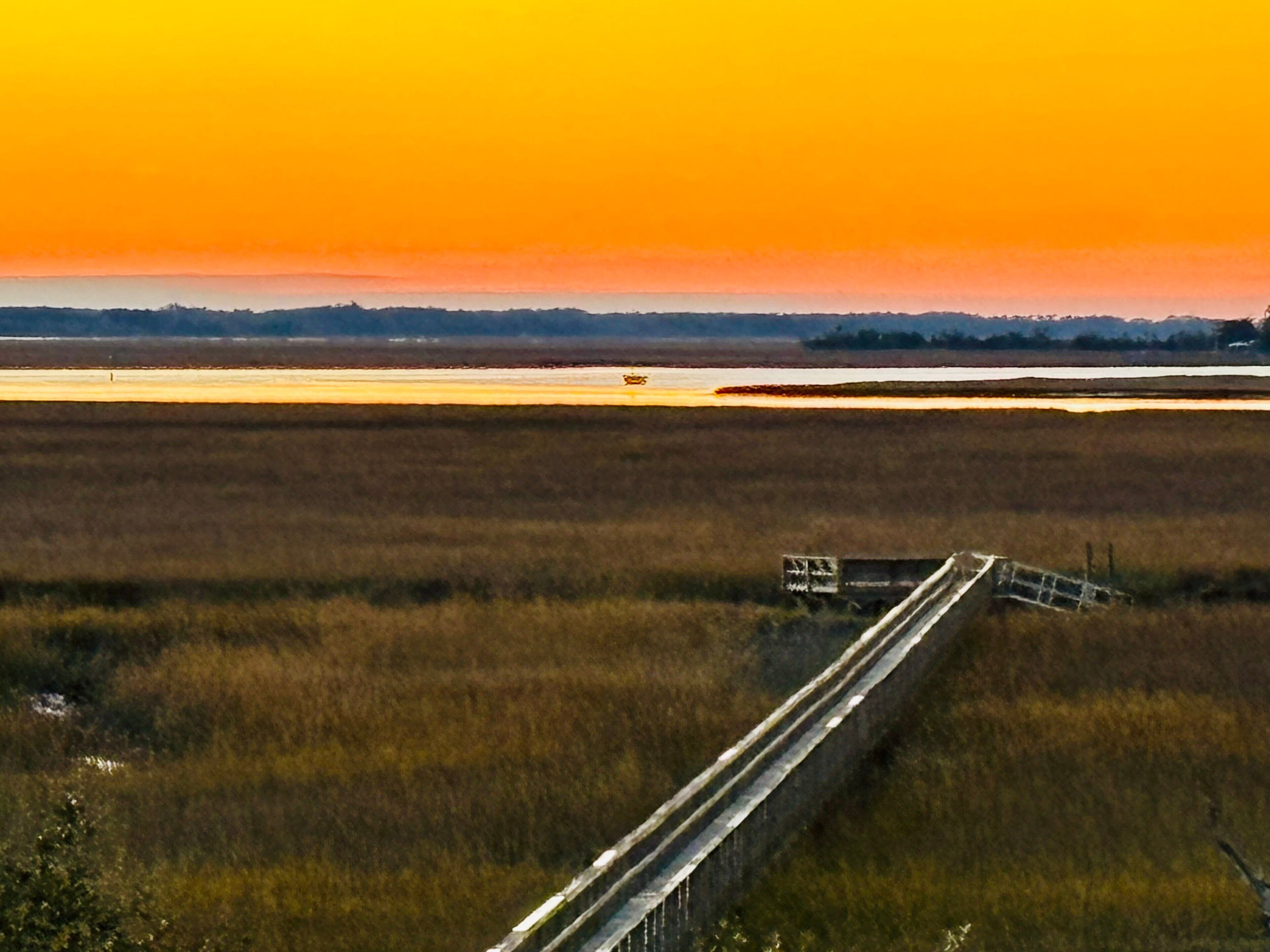 A bridge over a marshy landscape with a sunset in the background.