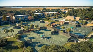 An aerial view of a residential area with multiple tennis courts, houses, and a large body of water in the background. - Stunning Gem! Amazing Marsh/Tidal Views. Amenity access included! (Seabrook Island)