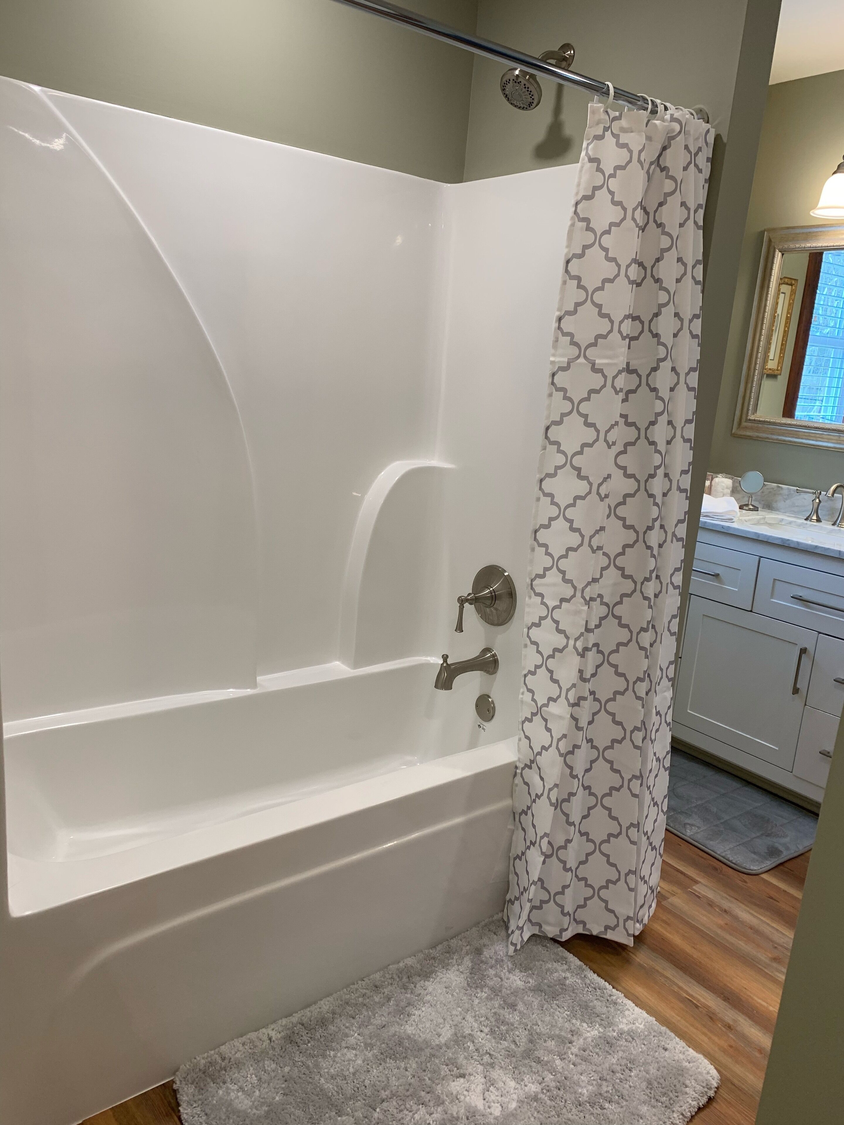 Ein Badezimmer mit einer weißen Badewanne, einem Duschvorhang mit geometrischem Muster, einem kleinen Spiegel und Holzboden.
