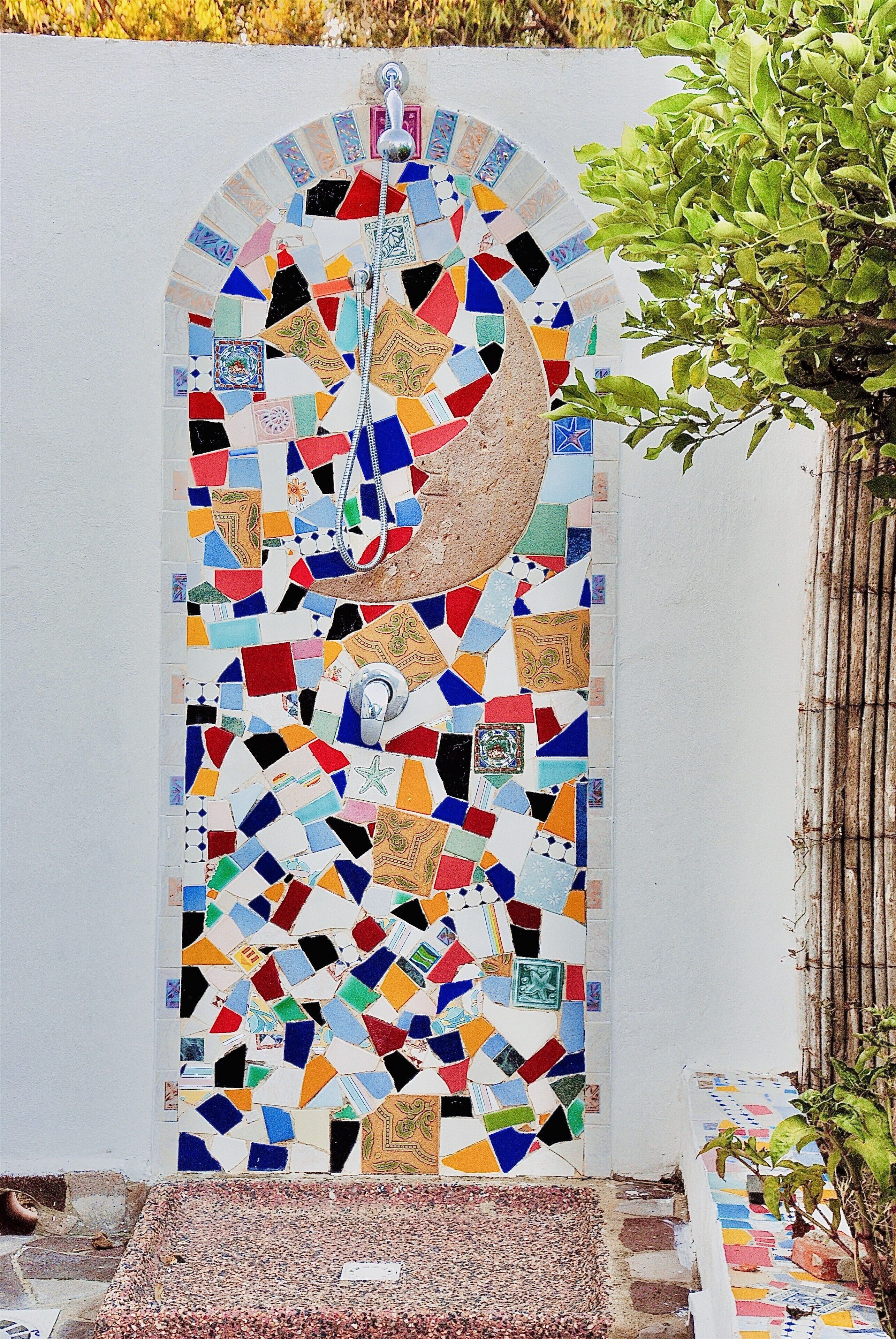 A mosaic-tiled shower enclosure with a crescent moon design, a showerhead, and a small plant to the right.