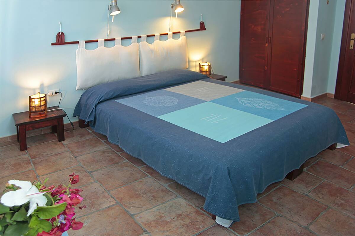 A neatly made bed with a blue bedspread and decorative pillows, two bedside lamps, and a wooden headboard.