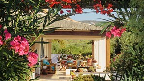 A covered outdoor seating area with tables and chairs, surrounded by lush greenery and flowering plants. - Alba B&B (Carloforte)