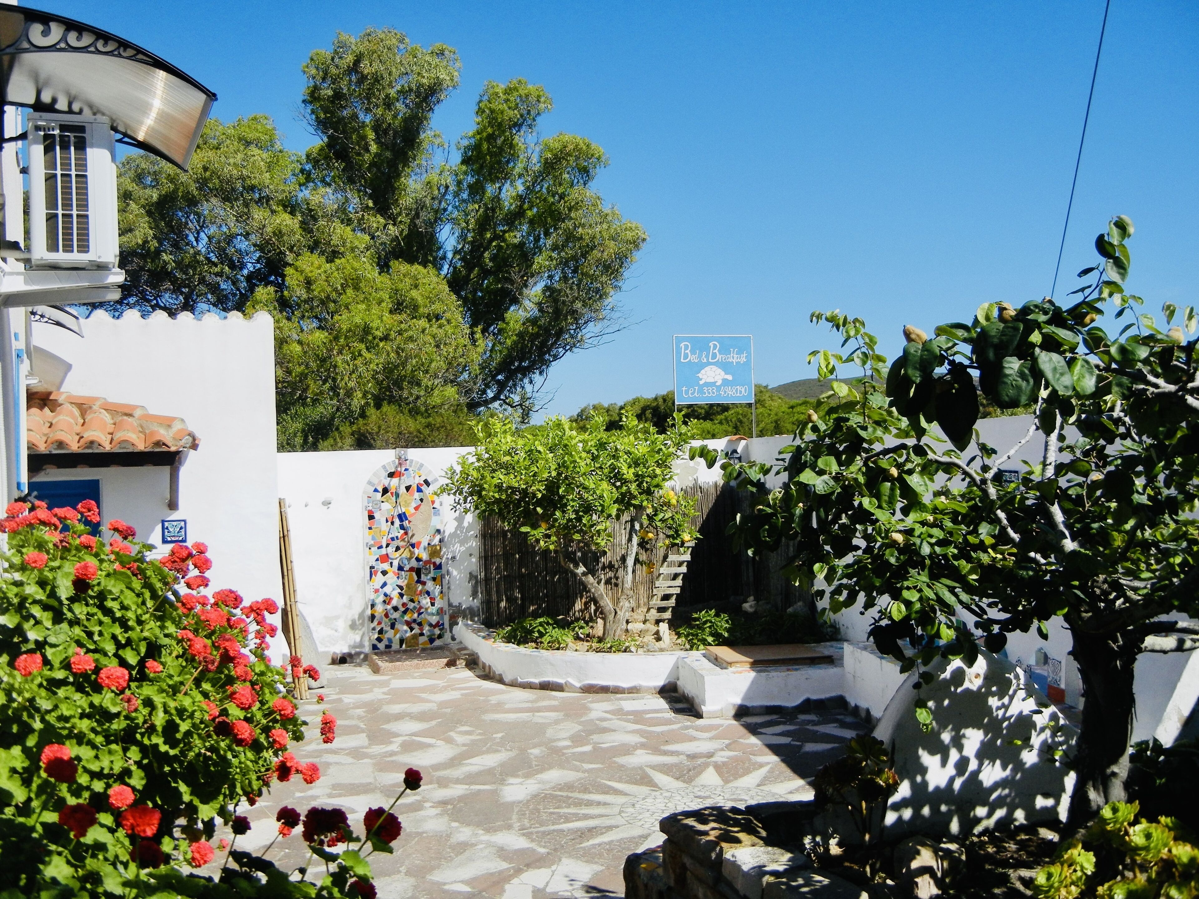 A courtyard with a tiled floor, a white building with a blue door, and a sign for 'B&B & Breakfast'.