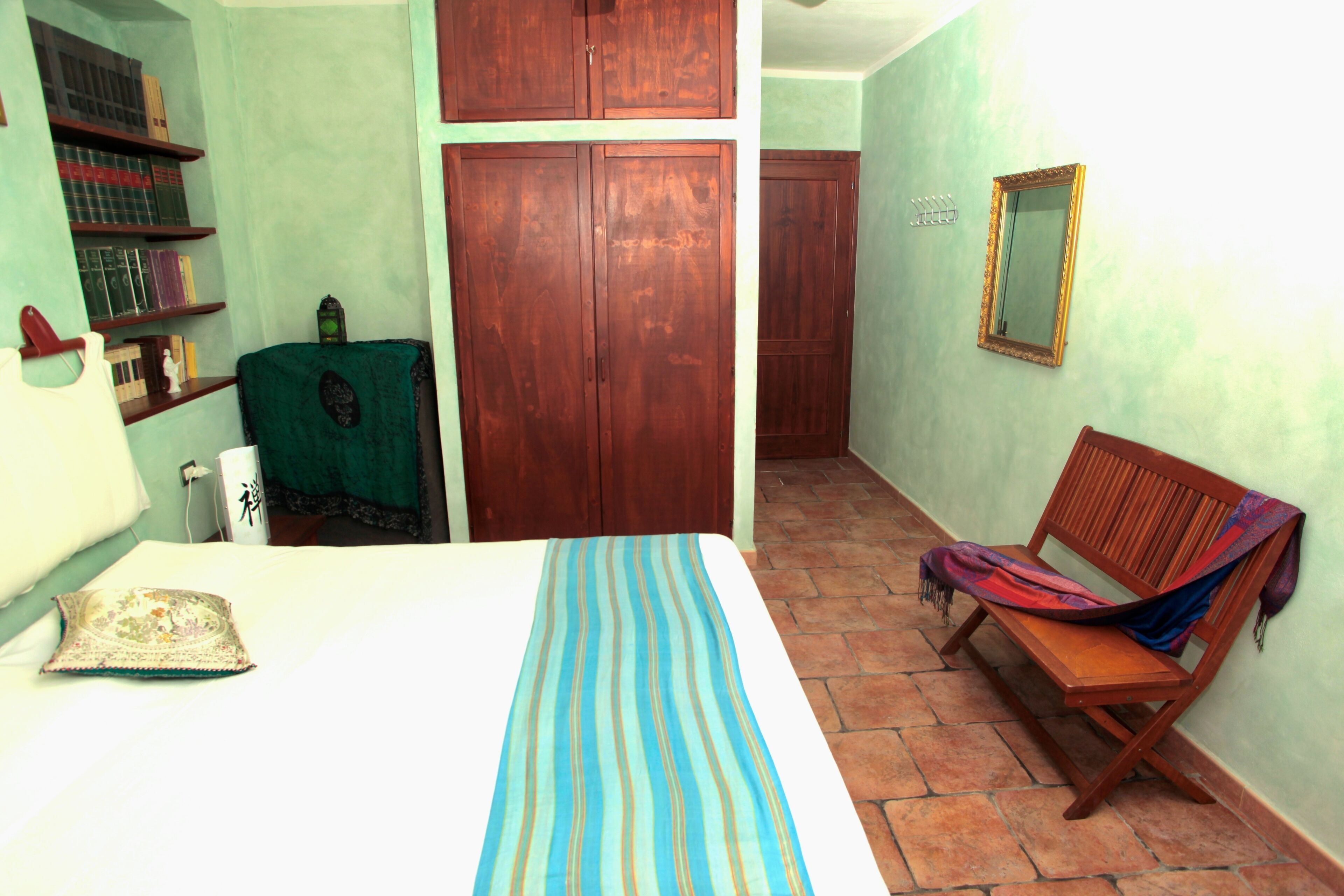 Un dormitorio con una cama, un armario de madera, un banco y una silla verde.