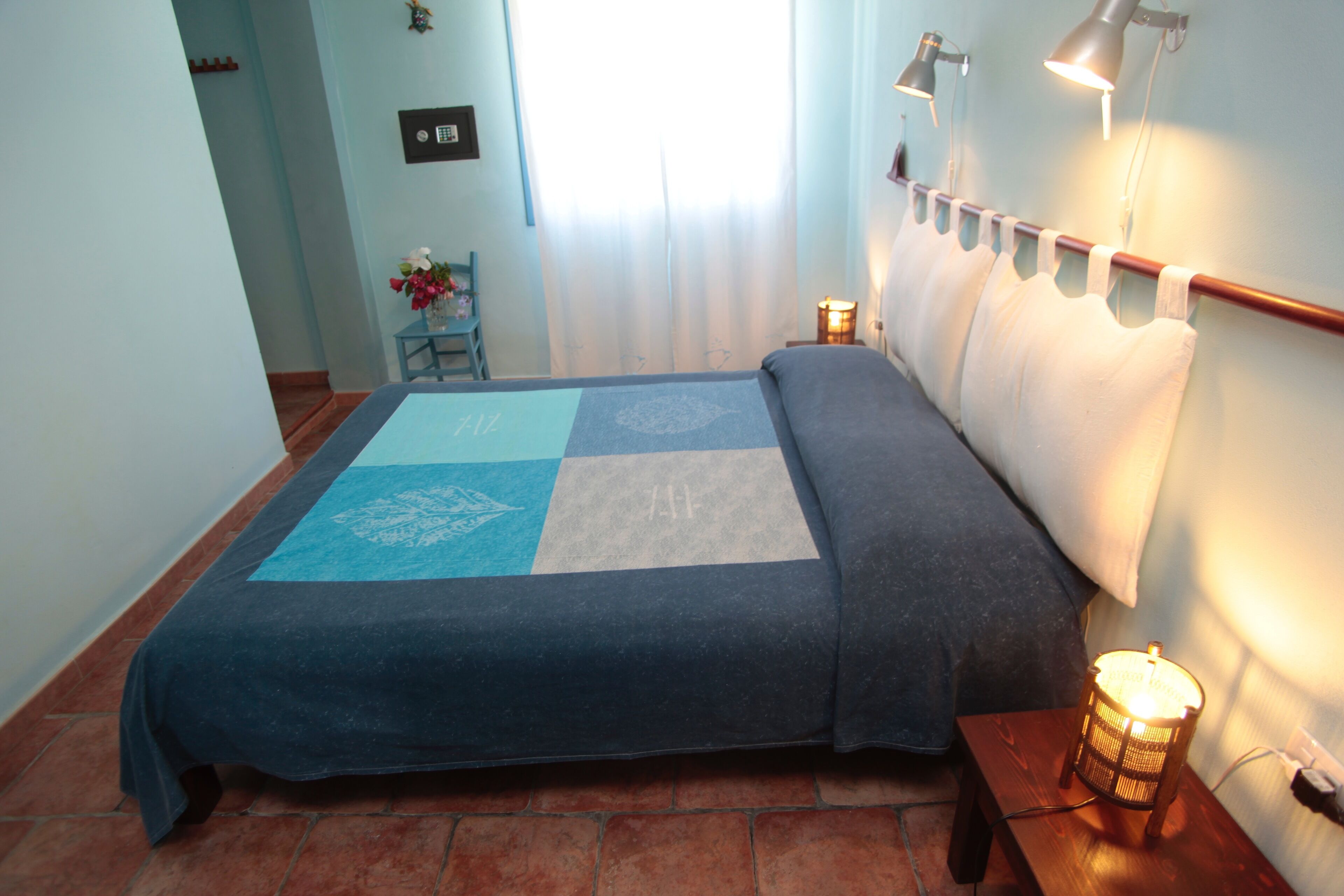 A bedroom with a bed, a bedside table with a lamp, a chair, and a window with curtains.