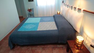 A bedroom with a bed, a bedside table with a lamp, a chair, and a window with curtains.