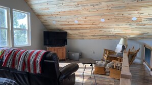 A cozy loft bedroom with a sloped ceiling, wooden flooring, a large bed, a TV, and a dining area. - Big Hole Valley cabin near river access (Wise River)