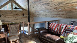 A cozy cabin interior with a wooden floor, a leather sofa, a wooden chair, a small table, and a window with a view of trees. - Big Hole Valley cabin near river access (Wise River)