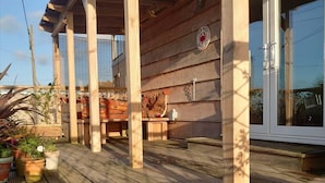Une terrasse en bois dotée d’un espace salon abrité, de plantes en pot et d’une grande fenêtre.