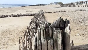 Une plage avec des structures en bois et une vue lointaine d’un bâtiment.