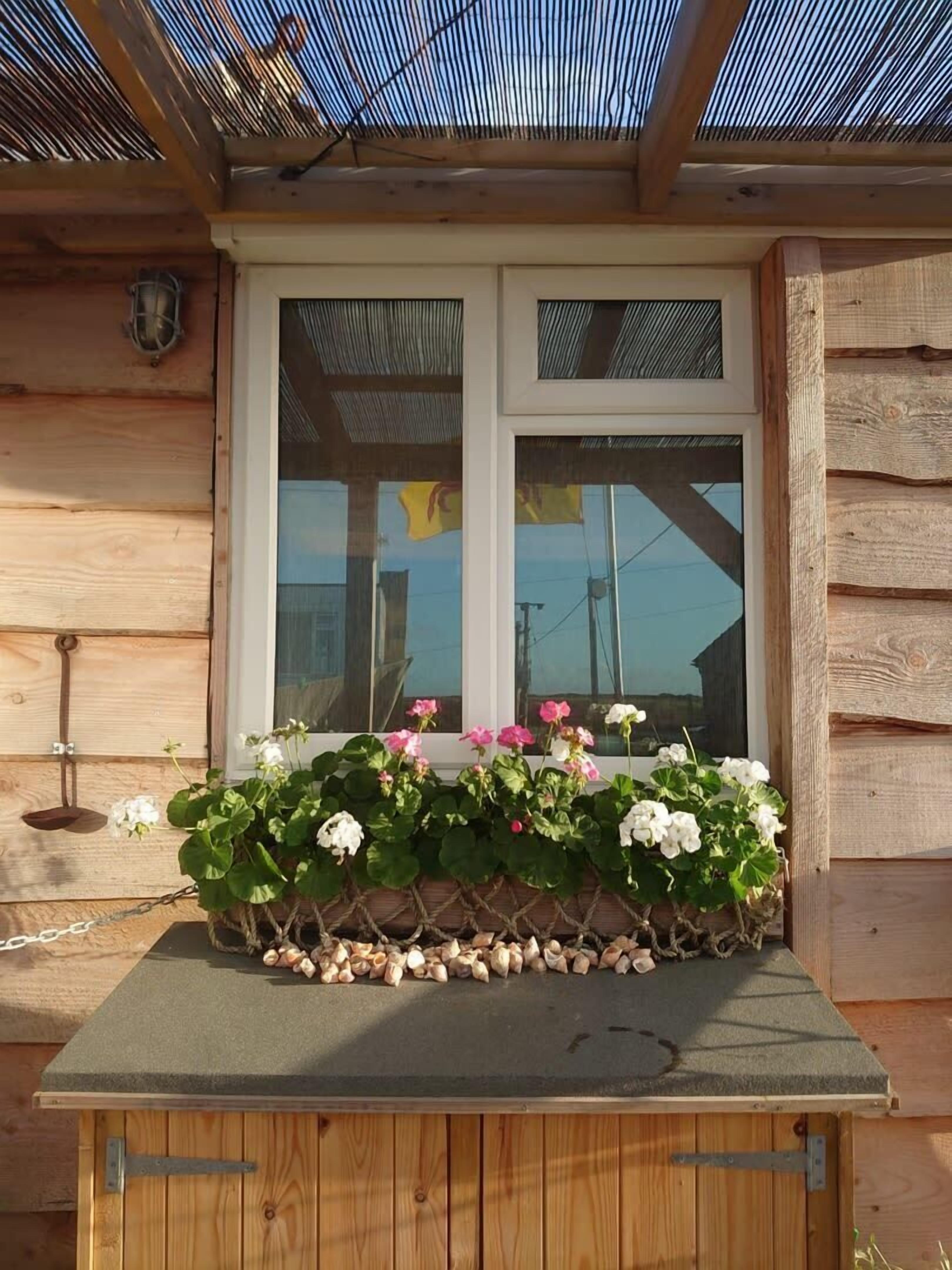 Une cabane en bois avec une fenêtre, une petite table sur laquelle est posée une plante, et un luminaire en métal.