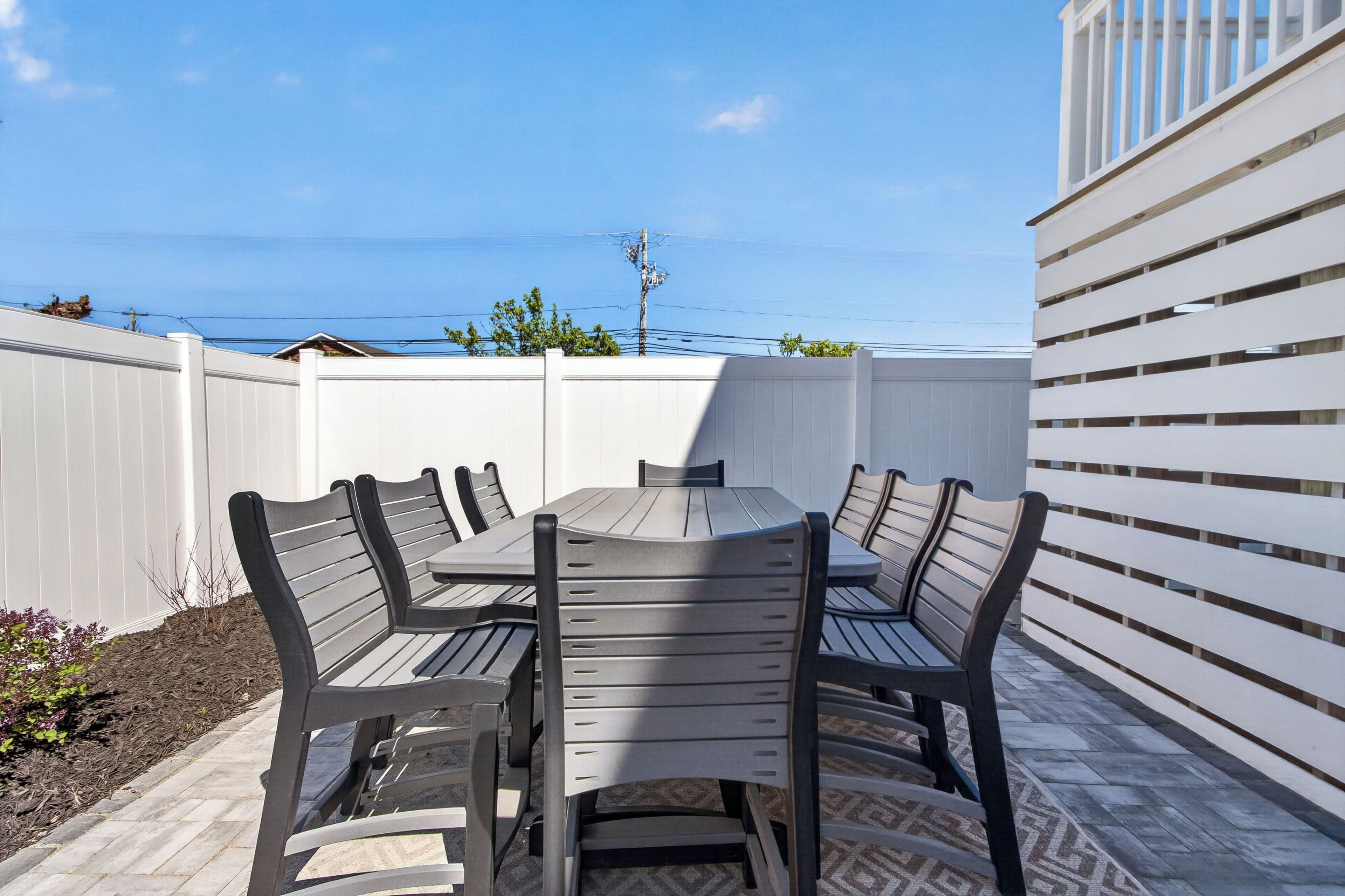 An outdoor dining area with a table and chairs, a white fence, and a view of the ocean.