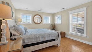 Un dormitorio con cama, mesitas de noche, lámpara, espejo y ventana con persianas.