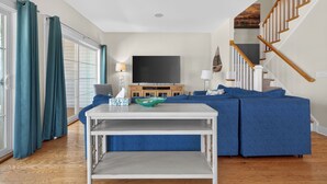 Una sala de estar con un sofá modular, un televisor de pantalla plana, una mesa de centro blanca y una escalera.