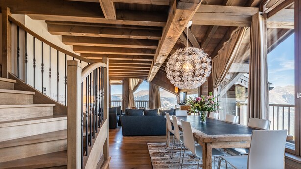 Un escalier en bois mène à un espace de vie comprenant une table à manger, des chaises et un luminaire suspendu.