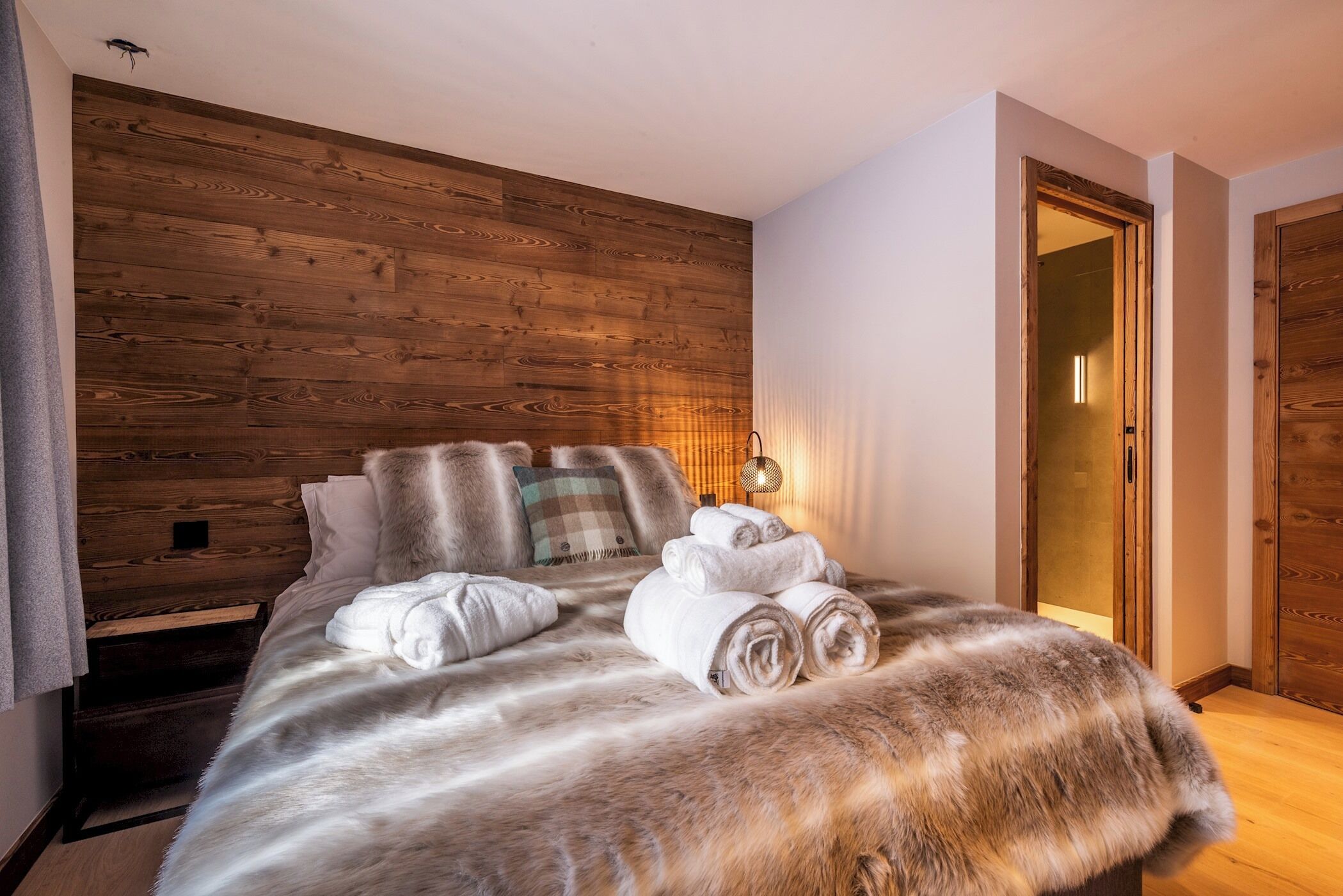 Een slaapkamer met een houten hoofdbord, een bont plaid en netjes opgevouwen handdoeken op het bed.