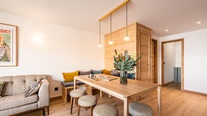 A modern living room with a sofa, a dining table with stools, and a wooden cabinet.