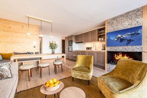 A modern kitchen with a built-in oven, a dining area with a wooden table and chairs, and a fireplace with a stone wall backdrop. - SIPO - Design apartment in brand-new residency (Huez)