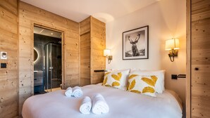 A hotel room with a wooden interior, a bed with white bedding and golden pillows, a framed deer picture on the wall, and two wall-mounted lamps.