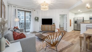 Una sala de estar moderna con un sofá, una mesa de centro y un televisor. Hay una zona de cocina con un refrigerador y una mesa de comedor.