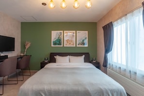 Habitación de hotel con una cama grande, un escritorio con silla, un televisor de pantalla plana y tres cuadros en la pared.