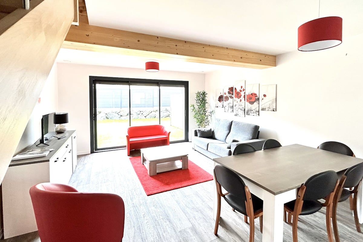 Un espacio de estar moderno con comedor, un sofá rojo, un sofá gris y una mesa de comedor con sillas.