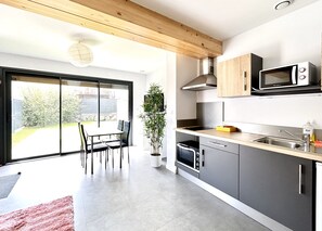 A modern kitchen with a sliding glass door to a patio, a microwave, a stove, and a dining area with chairs. - Résidence Montifault - gîtes du 2 au 3 pièces (Le Pallet)